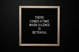 A black letterboard on a flat black background. The message reads, "There comes a time when silence is betrayal."